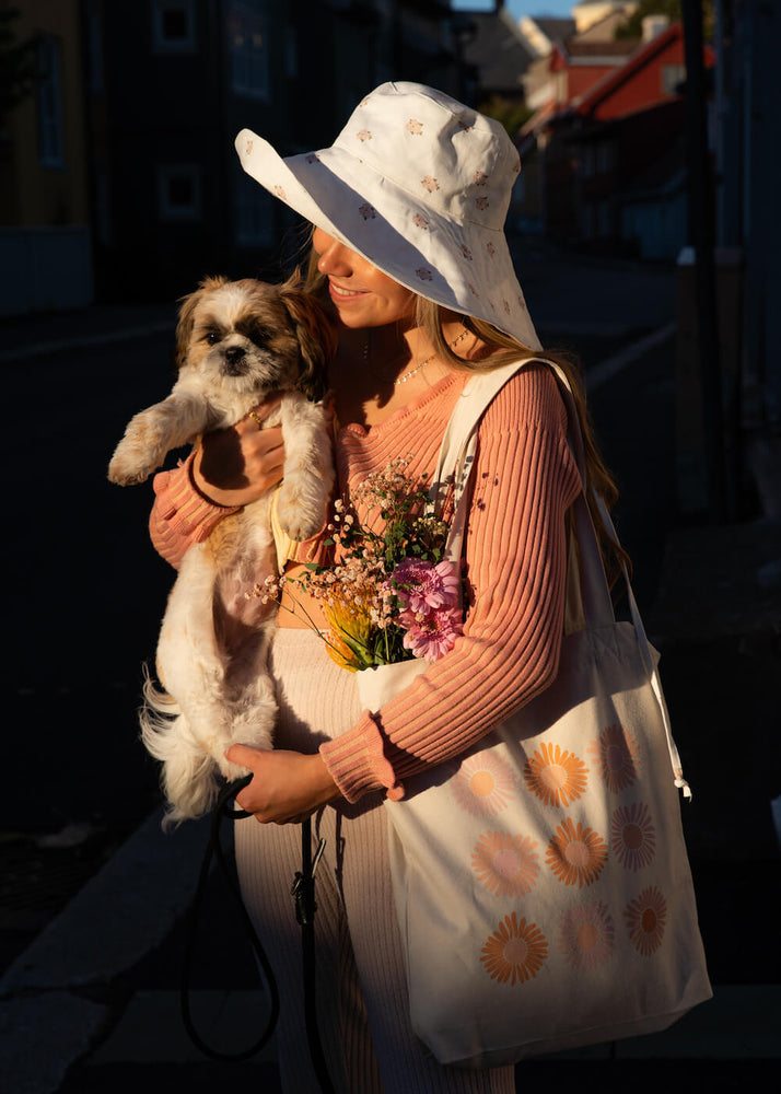 
            
                Last inn bildet i Gallery viewer, Mina står og holder hunden sin. På skulderen henger et hendlenett med motivet av ni blomster. 
            
        