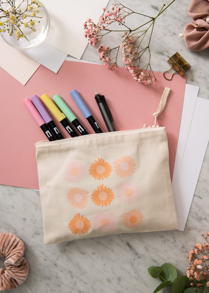 Flatlay bilde av en mappe med blomstermotiv som innholder ulike penner. Mappen har et motiv med ni ulike blomster.